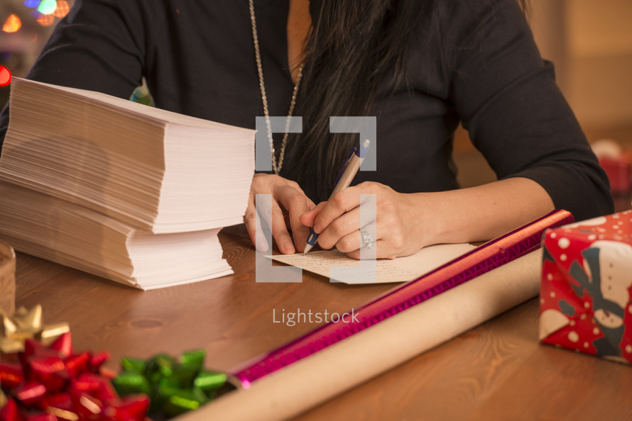 a woman addressing holidays cards and wrapping Christmas gifts 
