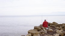 A fishman sits on a rock and looks out to sea.