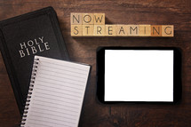 Bible and notebook on a wood background - now streaming 