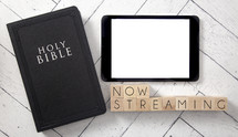 Bible and tablet on a white wood background - now streaming 