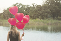 girl holding red Helium balloons by a lake 