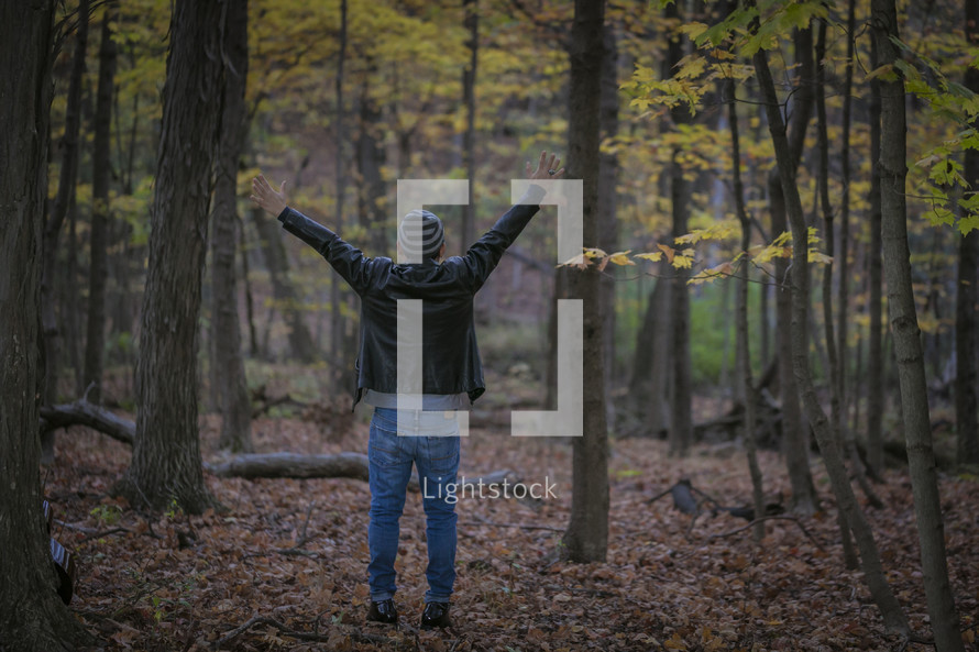 a man standing in a forest with arms raised 