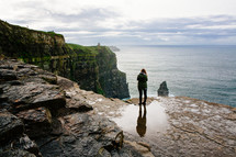 a woman standing at the edge of a sea cliff looking out over the ocean 
