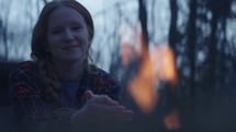 Young woman enjoying the warmth of a campfire at dusk