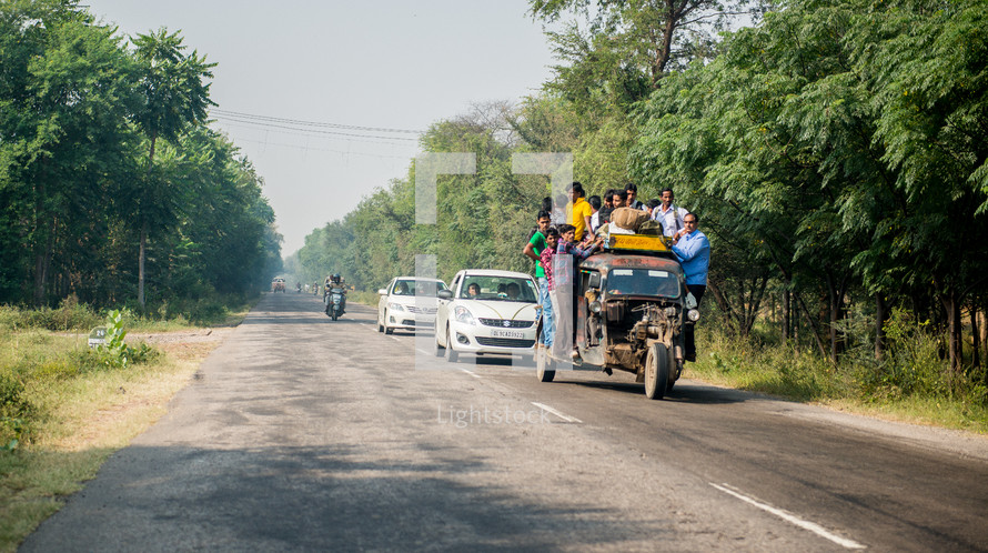 people loaded onto a crowded vehicle traveling on a road in India 
