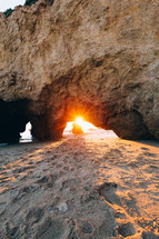 Sunrise seen through a rock arch on a sandy beach.