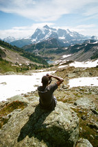 man with a camera taking a picture of melting snow on a mountain 