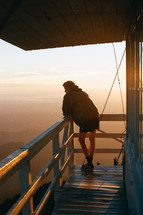 person on a deck overlooking fog over a mountain at sunrise 