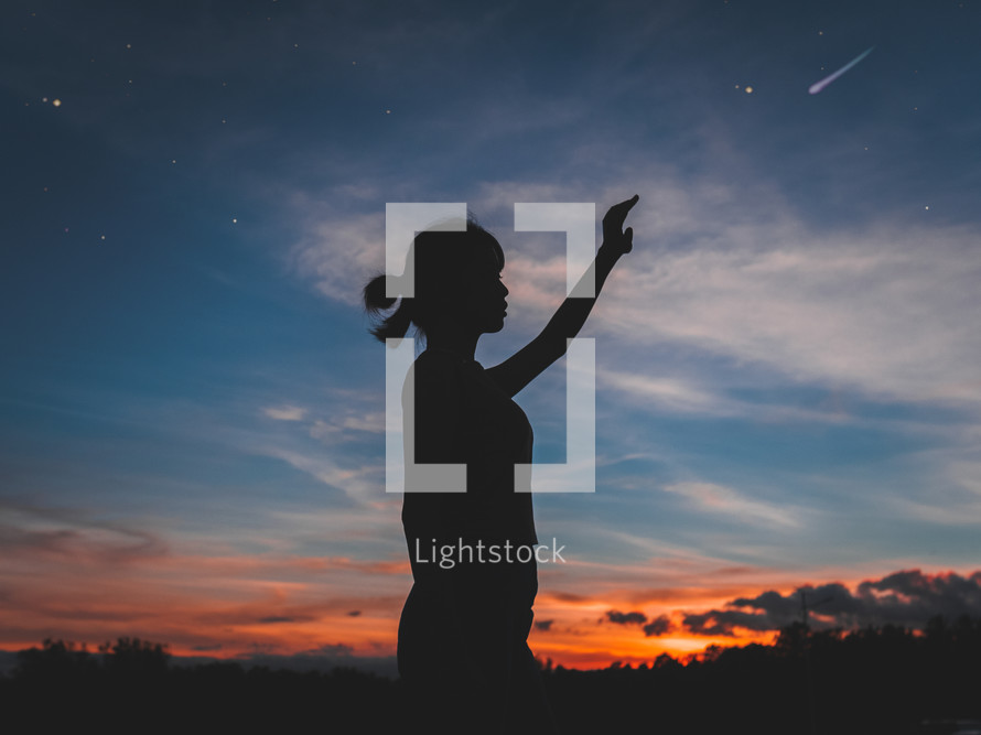 silhouette of a woman outdoors at sunset reaching for the stars 