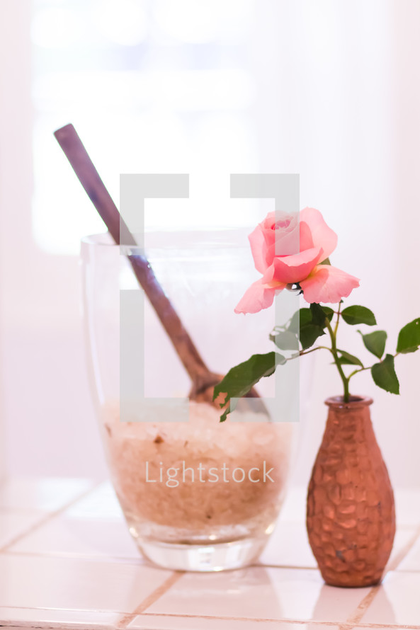 pink rose in a vase and bath salt in a cup 