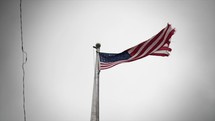 Tattered and worn American, USA flag blowing in cinematic slow motion in the wind in front of grey cloudy sky.