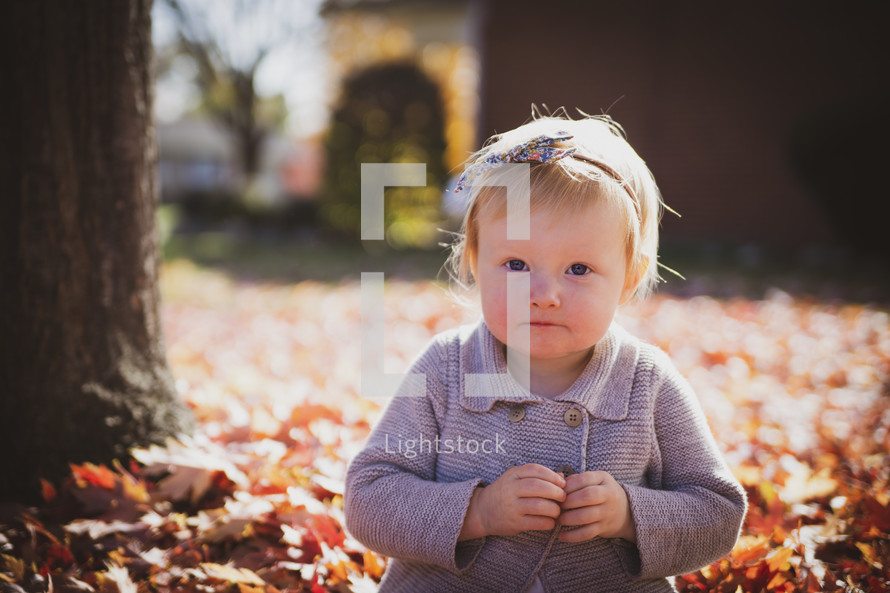 a shy little girl playing in fall leaves 