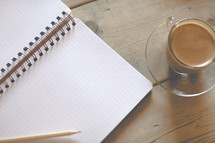 a pencil on the blank pages of a journal and coffee cup 