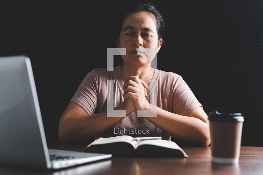 Asian woman praying with Bible and computer