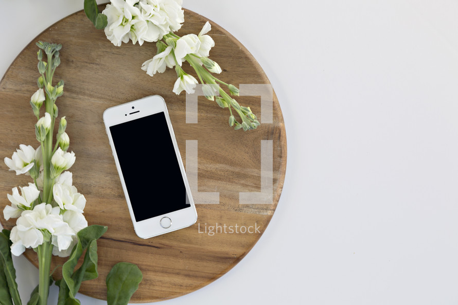 cellphone and white flowers on a cutting board against a white background 