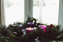 Advent wreath with one candle lit by a window