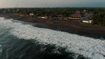 Drone view of ocean waves rolling onto a black sand beach.