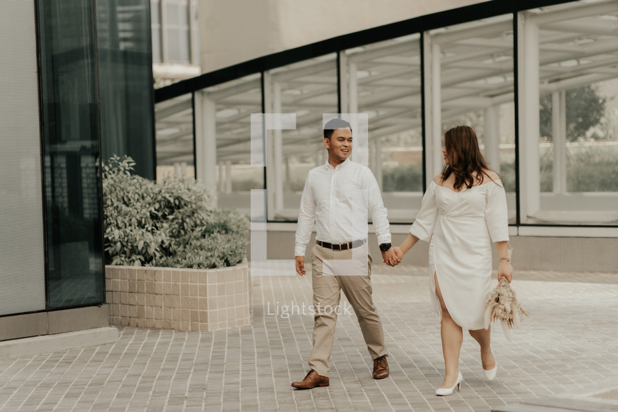 casual portrait of a bride and groom walking holding hands 