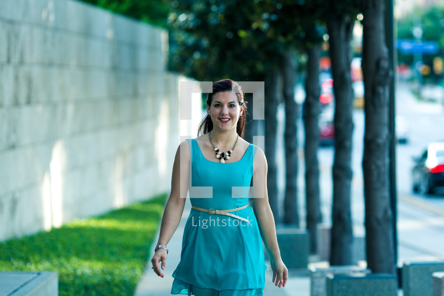 a woman in a blue dress walking down a sidewalk 