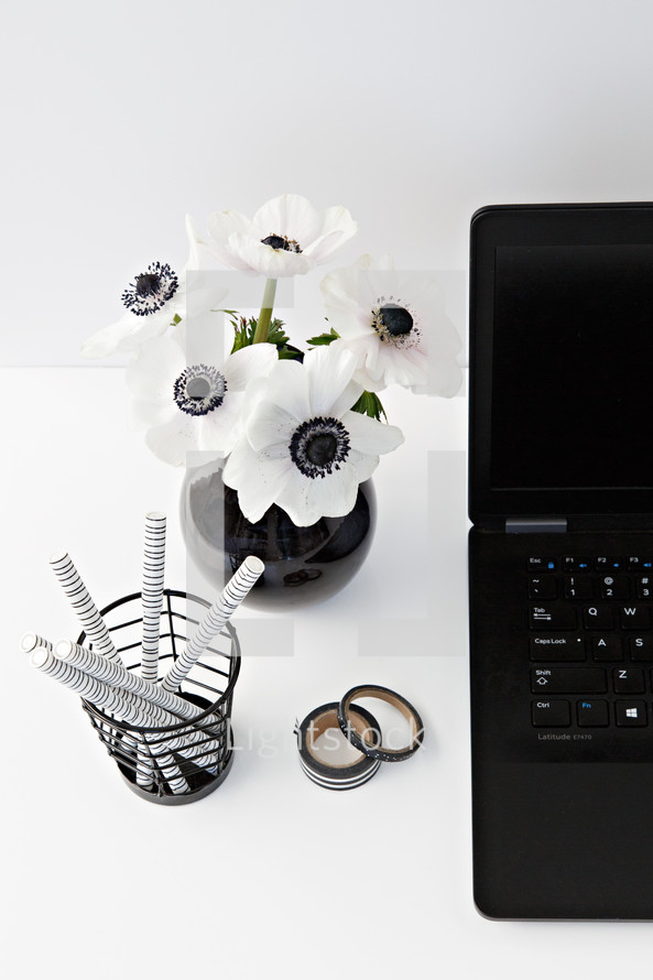 flowers in a black vase, laptop computer, journal, and pens on a desk 