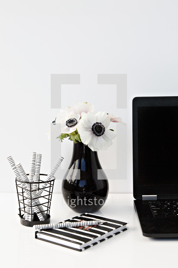  pens in a jar, journal, flowers in a vase, and laptop computer on a desk