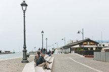 People sitting on steps on a paved pier.