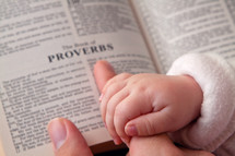 infants hand over mother's fingers and an open Bible