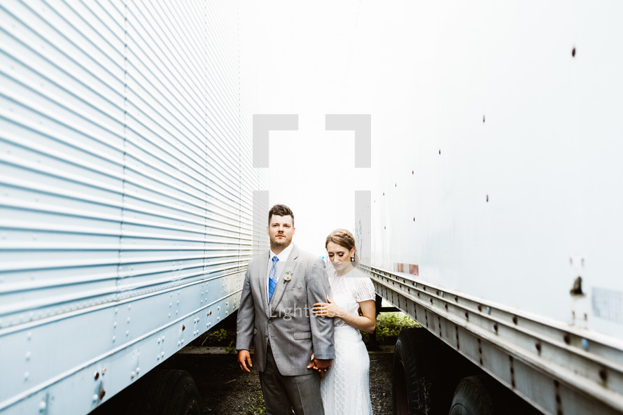 bride and groom standing between trucks 