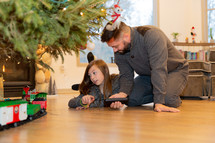 father and daughter setting up a train under a Christmas tree