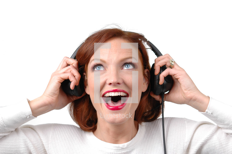 A woman listening to headphones with an excited look on her face.