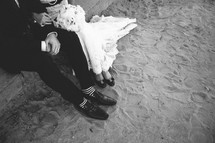 Bride and groom sitting on stone steps with shoes in the sand.