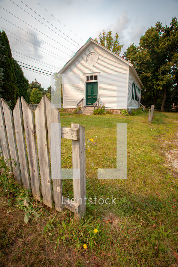 Quaint rural schoolhouse with wooden fence and yard vertical 