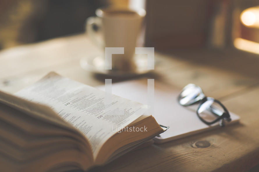 a notebook, reading glasses, coffee cup, and an open Bible on a desk 