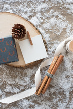 cinnamon sticks, ribbon, pine cones, wood, paper on snow 