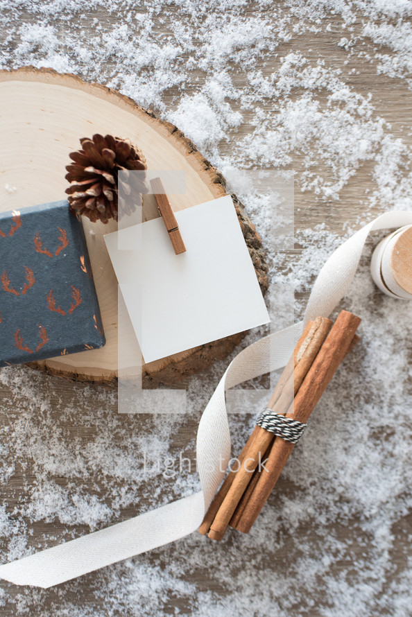 cinnamon sticks, ribbon, pine cones, wood, paper on snow 