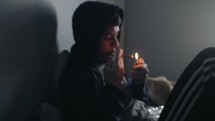 Young teenage boy sitting on his bed lighting and smoking a cigarette or doing drugs.