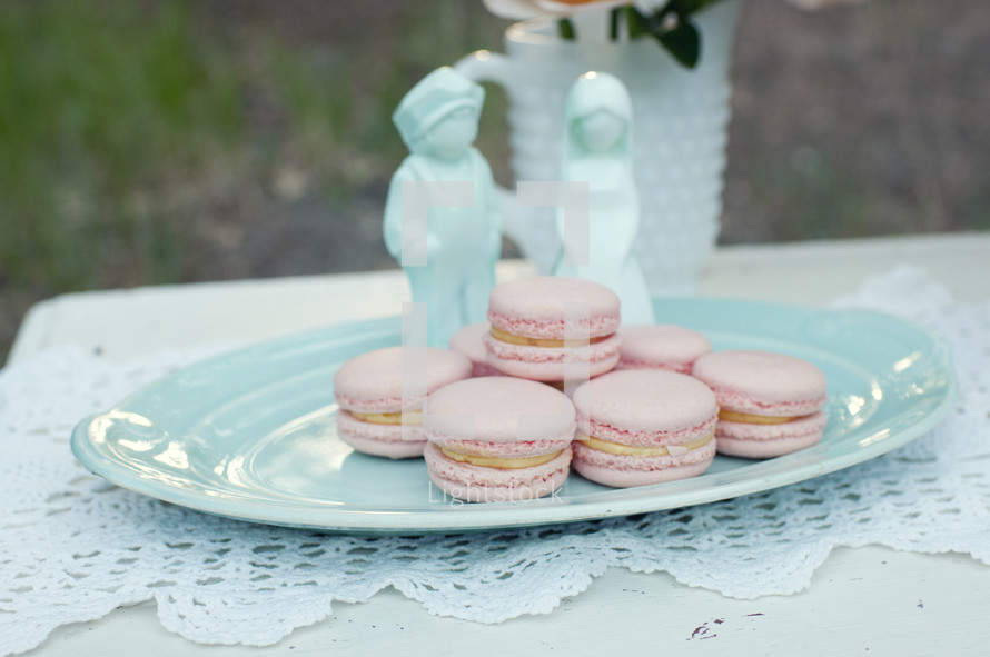 Pink macarons on a blue plate with bride and groom figurines.
