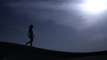 Man walking in middle eastern desert sunset in a desert nature landscape. Sand blowing in wind over desert sand dunes in evening desert sunset, sunlight in cinematic slow motion.