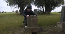 Sad, grieving man embracing family tombstone in cemetery crying in cinematic slow motion. 