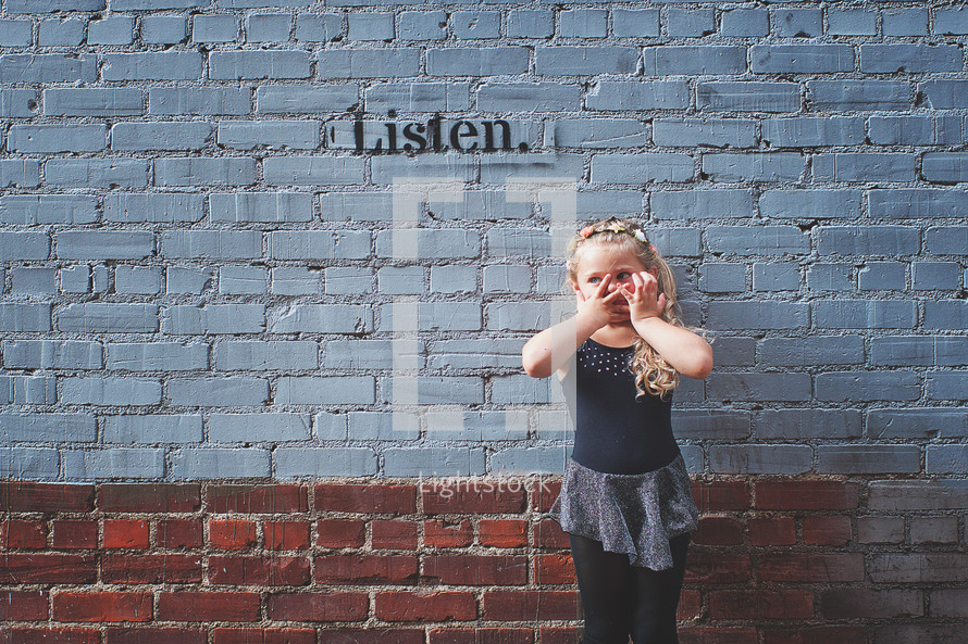 a little girl covering her mouth over the word listen 