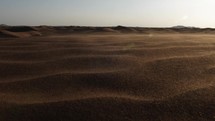 Middle eastern desert, nature landscape. Sand blowing in wind over desert sand dunes in evening desert sunlight in cinematic slow motion.