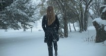 Woman in winter coat walking outside on Christmas, in winter snow as snowflakes fall in cinematic slow motion.