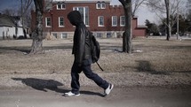 Young man, teenager with backpack and winter coat walking in cinematic slow motion. A young, teen boy walking to high school or young homeless man. 