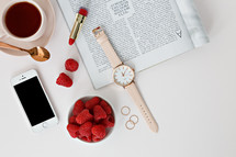 iPhone, red lipstick, Raspberries in a bowl, watch, magazine, rings, spoon, and coffee cup