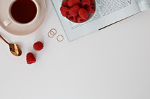 Raspberries in a bowl, magazine, rings, spoon, and coffee cup