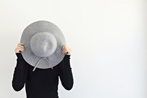 a woman hiding behind a hat 