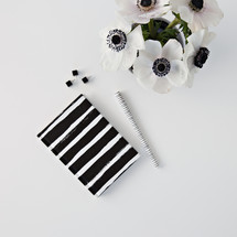 flowers in a black vase,  journal, and pens on a desk 