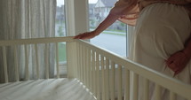 Third trimester pregnant woman looks over baby crib in preperation