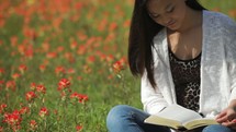 A girl sitting in a meadow of flowers reading a Bible outdoors 
