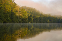 Evergreen trees and mist reflecting on still lake